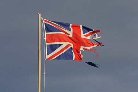 British flag or Union Jack torn and tattered flying in the winter by the sea in Italy representing the disaster of Brexitの写真素材