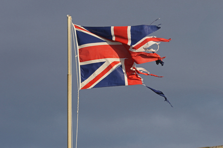 weather worn British flag or Union Jack torn and tattered flying in the winter by the sea in Italyの写真素材