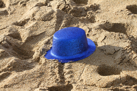 blue glittery party hat abandoned on the beach after a celebration or partyの写真素材