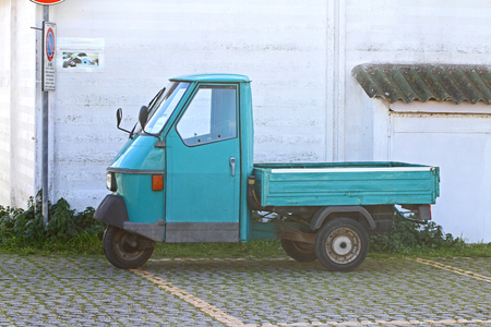 parked up mini Italian truck or pickup called an ape which means bee in English with three wheels in a car park by a wall near the sea in Italy in winter a commercial vehicleの写真素材