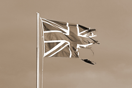 weather worn washed out and faded color image of a British flag or Union Jack torn and tattered flying in the winter by the sea in Italyの写真素材