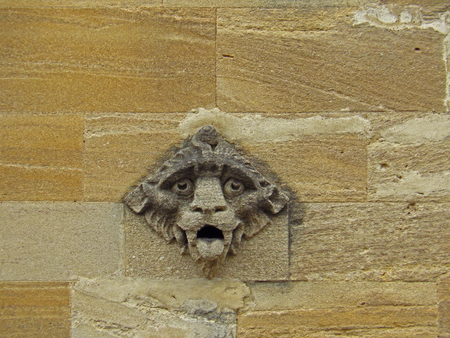 A weather worn or weather-beaten stone gargoyle or grotesque on the wall of a college in Oxford part of the university in sandstone or limestone from the Cotswold region of Oxfordshire in Englandのeditorial素材