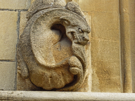 A weather worn or weather-beaten stone gargoyle or grotesque on the wall of a college in Oxford part of the university in sandstone or limestone from the Cotswold region of Oxfordshire in Englandのeditorial素材