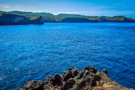 Picturesque ocean cove of Crystal Bay at sunset. Crashing waves, anchored boats, colorful sunset, tropical vibes located off the western coast of Nusa Penida, an island southeast of Bali, Indonesiaの写真素材