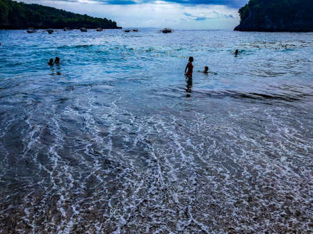 Picturesque ocean cove of Crystal Bay at sunset. Crashing waves, anchored boats, colorful sunset, tropical vibes located off the western coast of Nusa Penida, an island southeast of Bali, Indonesiaの写真素材