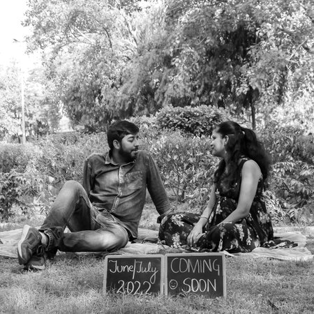 Indian couple posing for maternity baby shoot. The couple is posing in a lawn with green grass and...
