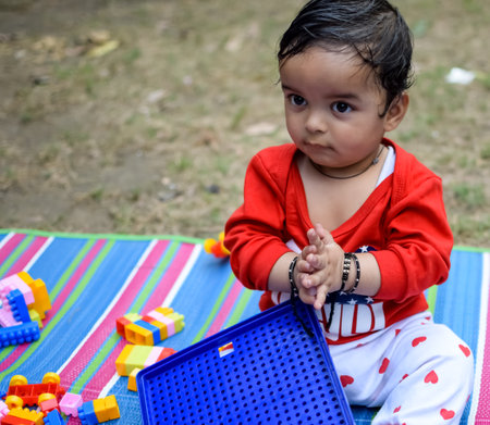 Cute little Indian infant sitting enjoying outdoor shoot at society park in Delhi, Cute baby boy sitting on colourful mat with grass around, Baby boy outdoor shootの写真素材