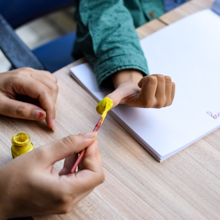 Smart Indian little boy perform thumb painting with different colourful water colour kit during the summer vacations, Cute Indian Kid doing colourful thumb painting drawing on wooden tableの写真素材