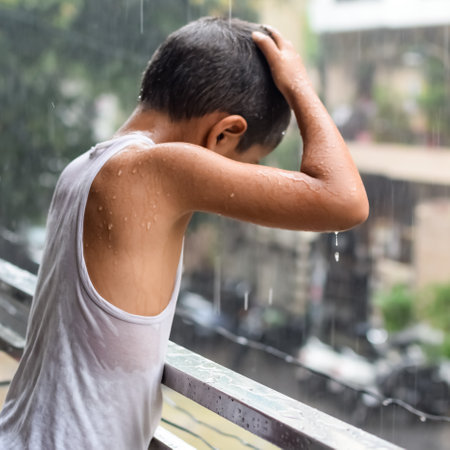 Little kid playing in summer rain in house balcony, Indian smart boy playing with rain drops during monsoon rainy season, kid playing in rainの写真素材