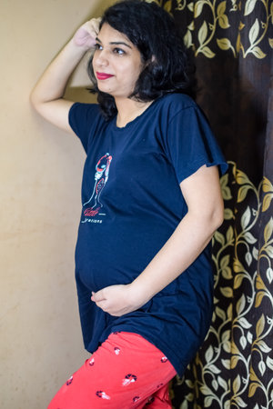 A pregnant Indian lady poses for indoor pregnancy shoot and hands on belly, Indian pregnant woman...