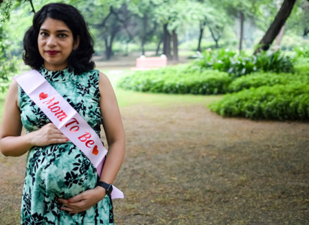 A pregnant Indian lady poses for outdoor pregnancy shoot and hands on belly, Indian pregnant woman puts her hand on her stomach with a maternity dress at society park, Pregnant outside maternity shootの写真素材