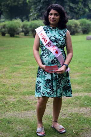 A pregnant Indian lady poses for outdoor pregnancy shoot and hands on belly, Indian pregnant woman puts her hand on her stomach with a maternity dress at society park, Pregnant outside maternity shootの写真素材