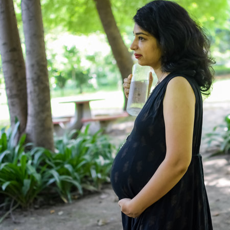 A pregnant Indian lady poses for outdoor pregnancy shoot and hands on belly, Indian pregnant woman puts her hand on her stomach with a maternity dress at society park, Pregnant outside maternity shootの写真素材