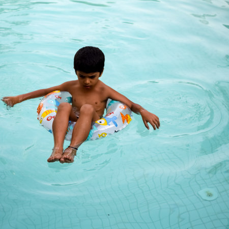 Happy Indian boy swimming in a pool, Kid wearing swimming costume along with air tube during hot summer vacations, Children boy in big swimming pool.の写真素材