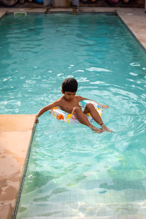 Happy Indian boy swimming in a pool, Kid wearing swimming costume along with air tube during hot summer vacations, Children boy in big swimming pool.の写真素材
