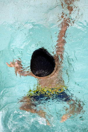 Happy Indian boy swimming in a pool, Kid wearing swimming costume along with air tube during hot...
