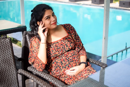 A pregnant Indian lady poses for outdoor pregnancy shoot and hands on belly, Indian pregnant woman puts her hand on her stomach with a maternity dress at society park, Pregnant outside maternity shootの写真素材