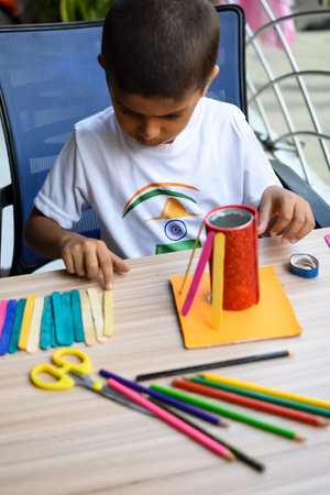 Smart Indian little boy performing best out of waste activity with different colourful objects during the summer vacations, Cute Indian Kid doing best our of waste activity at home on wooden tableの写真素材