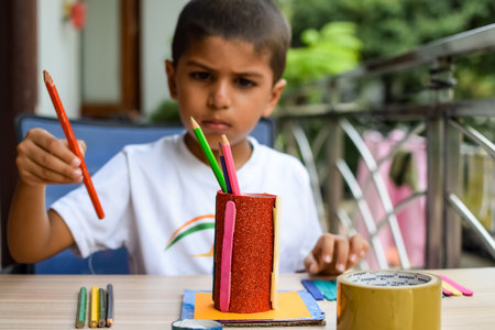 Smart Indian little boy performing best out of waste activity with different colourful objects during the summer vacations, Cute Indian Kid doing best our of waste activity at home on wooden tableの写真素材