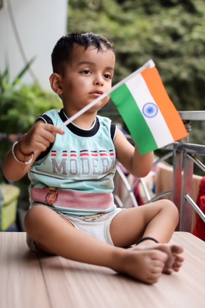 Cute boy holding national flag in his hands at home balcony. Bright portrait of happy child sitting...