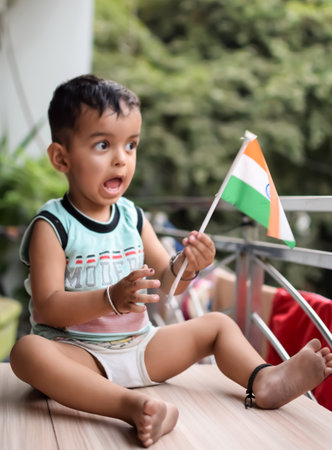 Cute boy holding national flag in his hands at home balcony. Bright portrait of happy child sitting on the table with flagの写真素材