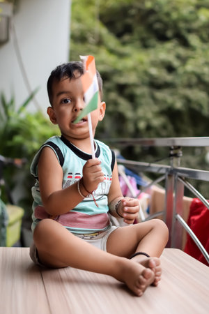 Cute boy holding national flag in his hands at home balcony. Bright portrait of happy child sitting...