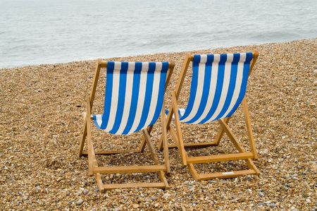 Two blue and white striped deckchairs on a pebble beach by the sea