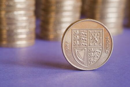 One pound coin in front of stacks of several coins against purple backgroundの写真素材