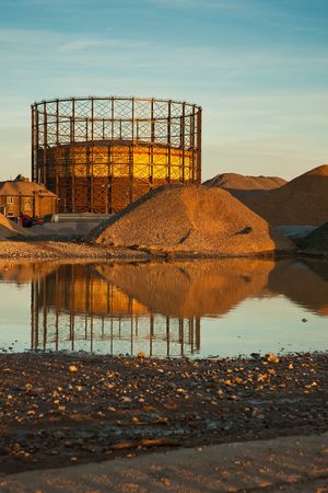 Gas reservoir and mounds of gravel with reflection at sunsetの写真素材
