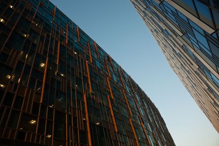 Two modern buildings with metal and glass facades at sunset against clear blue skyの写真素材