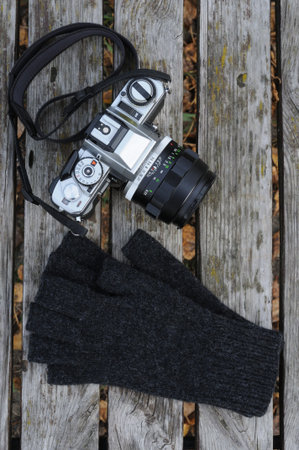 Top view of analog camera, knitted gloves with open fingers on wooden background. Autumn concept. Knitted gloves for photographers.の写真素材