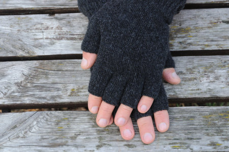 Male hands in black woolen gloves with open fingers on a wooden bench. Top view. Handmade knitted things.の写真素材