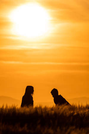 silhouettes of girl and boy in a cereal field at sunset with a sky of fireの写真素材