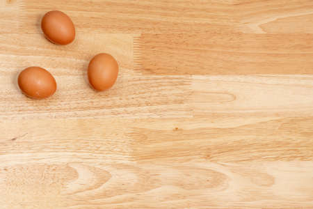 Three eggs on the upper left corner of the wooden table with copy space
