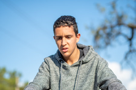 Half body shot of latin teenage boy with black hair wearing gray sweater on a sunny dayの写真素材