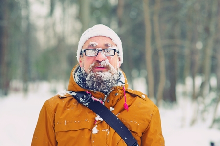 Closeup portrait of happy young bearded man in cold weather in the winter forest at sunset. Fun guy smiles. Face, beard , mustache, and glasses misted, covered with frost.の写真素材
