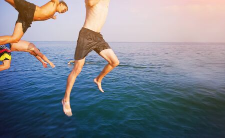 Group of happy crazy people having fun jumping in the sea water from boat. Friends jump in mid air on sunny day summer pool party at diving holiday. Travel vacation, friendship, youth holiday conceptの写真素材