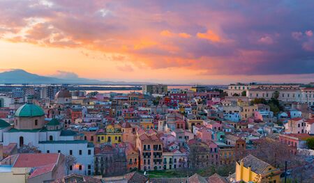 Sunset on Cagliari, panorama of the old city center with traditional colored houses, mountains and beautiful yellow-pink clouds in the sky, Sardinia Island, Italyの写真素材