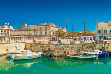 Syracuse - April 2019, Italy: Cityscape of Syracuse and a small Island Ortygia, historical part of the city. Colorful boats lying on water near a stone pierのeditorial素材