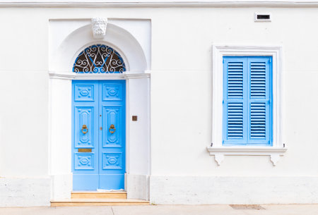 Facade of an old Maltese residential building with a blue wooden door and a window with closed shuttersの写真素材