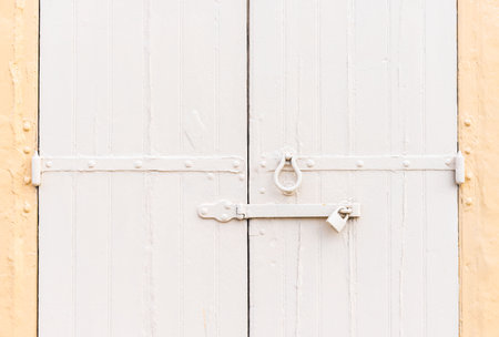 Closed vintage wooden gates made of wooden planks and an iron lock on it painted in beige and ochre colorsの写真素材
