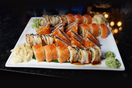 Eating sushi rolls. Japanese food restaurant, sushi maki gunkan roll plate or platter set. Closeup of hand with chopsticks taking roll. Ginger, soy, wasabi. Sushi at black rustic wood background.の写真素材