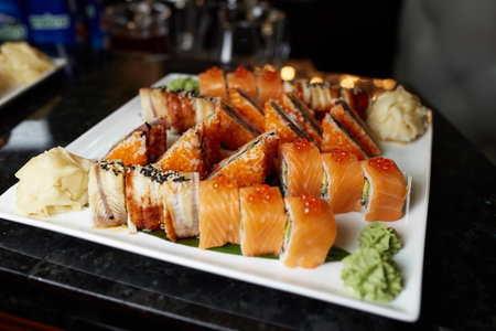Eating sushi rolls. Japanese food restaurant, sushi maki gunkan roll plate or platter set. Closeup of hand with chopsticks taking roll. Ginger, soy, wasabi. Sushi at black rustic wood background.の写真素材