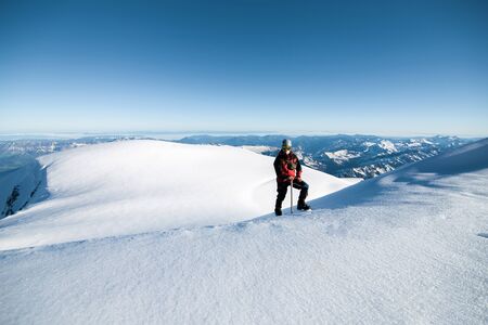 climber in a red jacket climbs a mountain against a blue skyの写真素材