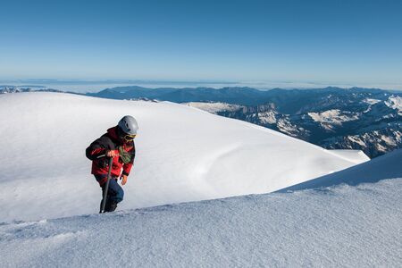 climber in a red jacket climbs a mountain against a blue skyの写真素材