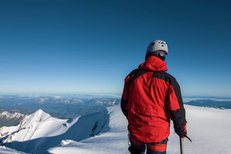 climber in a red jacket stands on top of a mountain against a blue skyの写真素材
