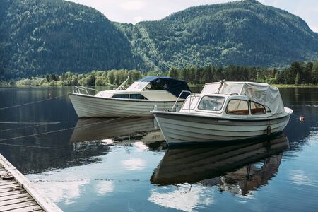 boats in pristan on a mountain river in norway against a blue sky with clouds in sunny weatherの写真素材