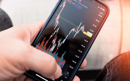 Stock market investment app in hand. Telephone with a stock chart. Screen close-upの写真素材