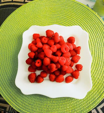 Big pile of fresh raspberries in white bowl isolated on light green background