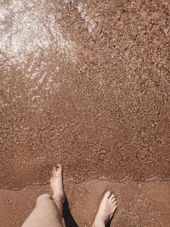 A man stands by the sea, his feet washed by the waves. Top down view.の写真素材